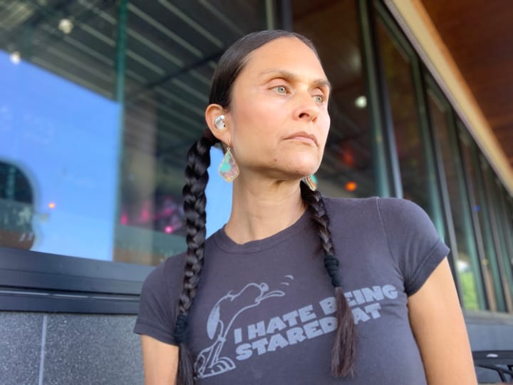 Elsie Escobar looking off to the side, wearing braids. T-shirt is slate gray with Snoopy sticking out his tongue. Words on the t-shirt say "I hate being stared at"